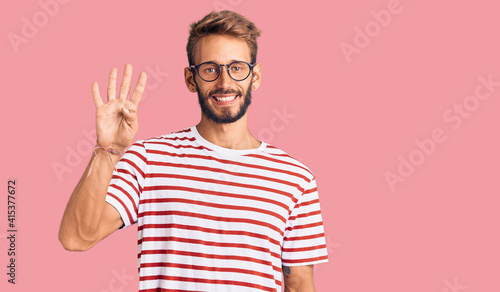 Handsome blond man with beard wearing casual clothes and glasses showing and pointing up with fingers number four while smiling confident and happy.