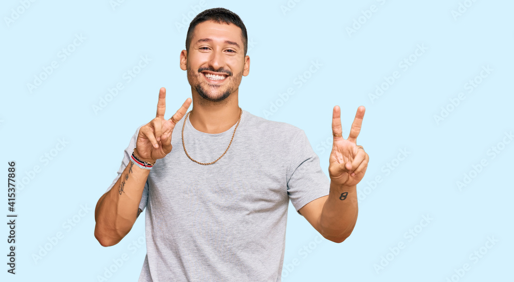 Handsome man with tattoos wearing 90s style smiling looking to the camera showing fingers doing victory sign. number two. Handsome man with tattoos wearing 90s style smiling looking to the camera showing fingers doing victory sign. number two.