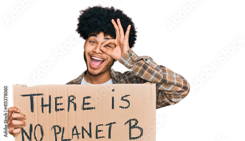 Young african american man with afro hair holding there is no planet b banner smiling happy doing ok sign with hand on eye looking through fingers © Krakenimages.com