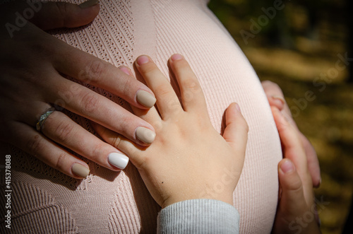 Close-up of a pregnant belly of a young mom, her and her baby hand on it