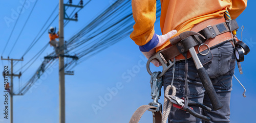 Photography Rear view of electrician with safety belt and work tools is preparing to work on