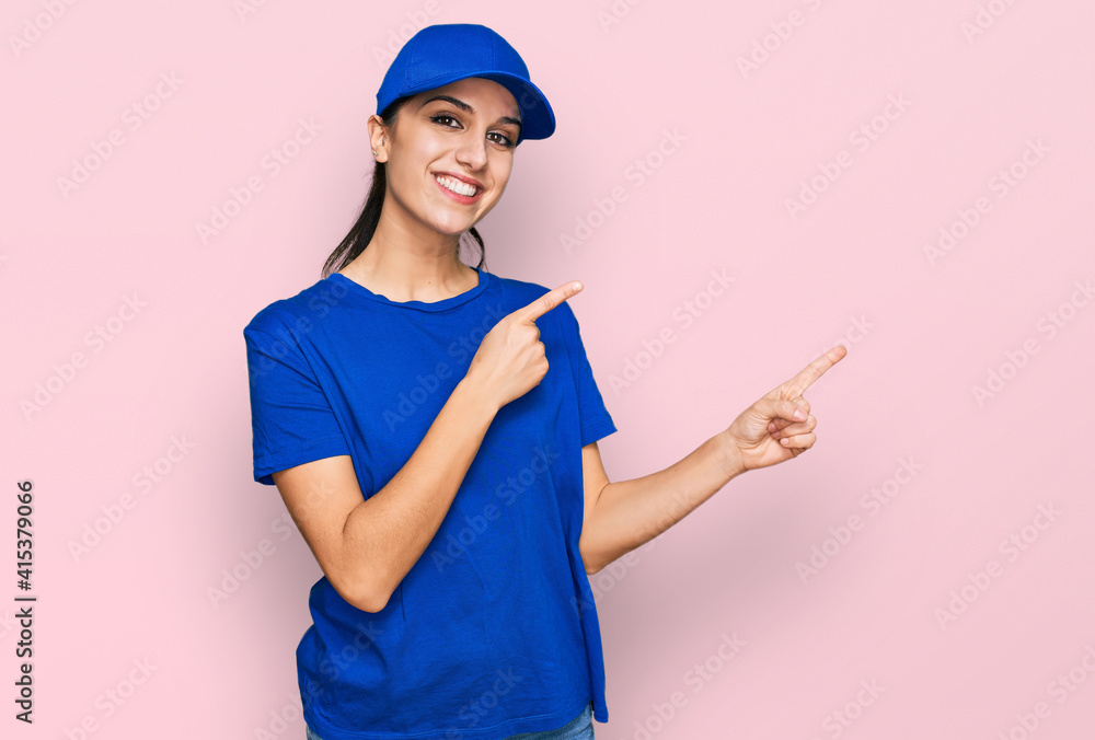 Young hispanic girl wearing delivery courier uniform smiling and looking at the camera pointing with two hands and fingers to the side.
