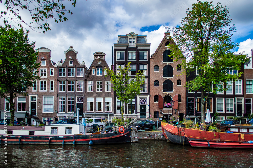 Amsterdam, Netherlands - July 7, 2019: Traditional Dutch houseboats and brick stone buildings along the canals in Amsterdam, the Netherlands