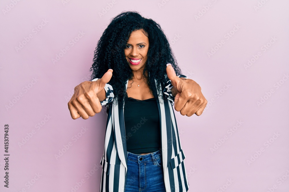 Middle age african american woman wearing casual clothes approving doing positive gesture with hand, thumbs up smiling and happy for success. winner gesture.