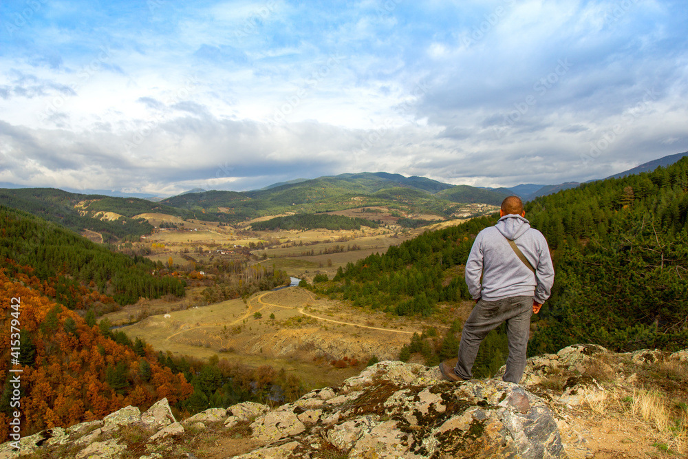 A man at the top of the mountain looks into the distance, against the background of mountains, sky and river. Clear sunny weather in the mountains