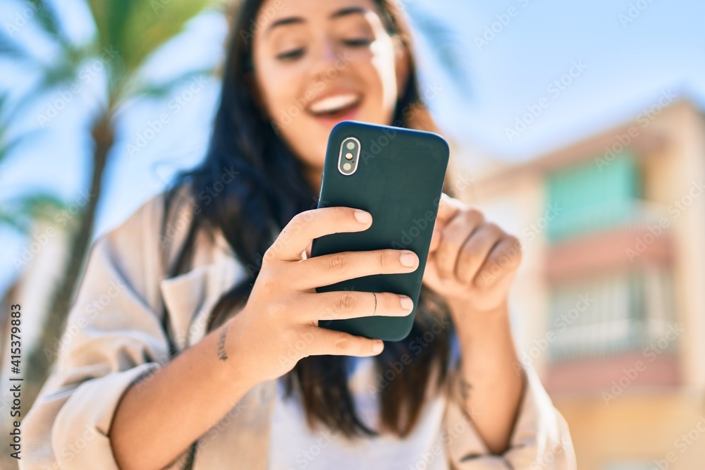 Young hispanic woman smiling happy using smartphone at the city.