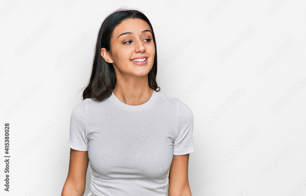 Young hispanic girl wearing casual white t shirt looking away to side with smile on face, natural expression. laughing confident. Young hispanic girl wearing casual white t shirt looking away to side with smile on face, natural expression. laughing confident.