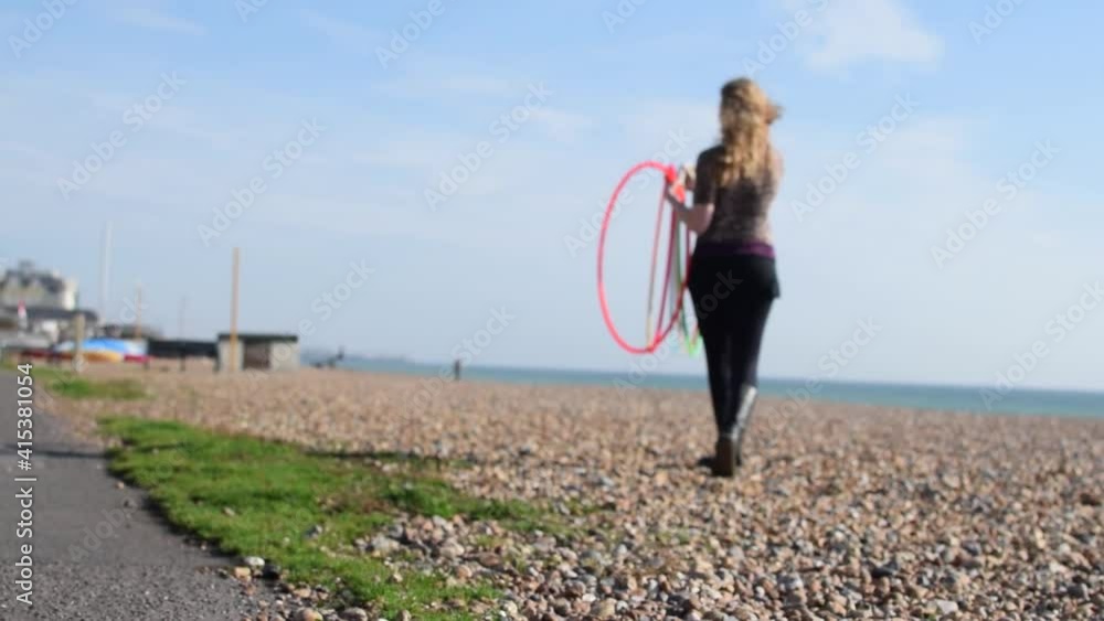 Una mujer rubia recogiendo unos aros de hula hoop del suelo de una playa en un día soleado