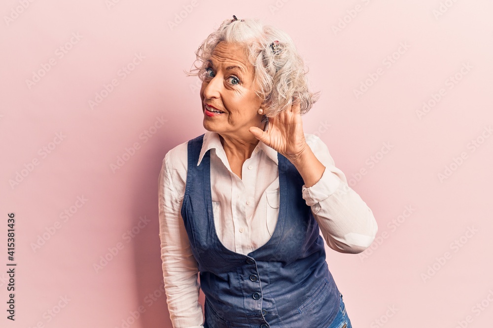 Senior grey-haired woman wearing casual clothes smiling with hand over ear listening and hearing to rumor or gossip. deafness concept. Senior grey-haired woman wearing casual clothes smiling with hand over ear listening and hearing to rumor or gossip. deafness concept.