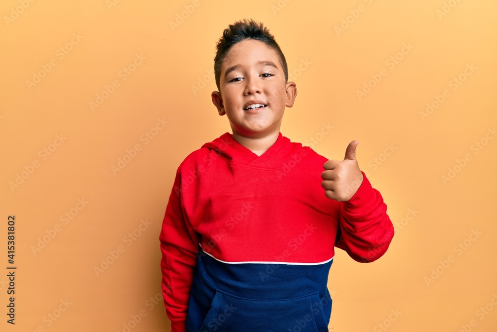 Little boy hispanic kid wearing casual sweatshirt smiling happy and positive, thumb up doing excellent and approval sign Little boy hispanic kid wearing casual sweatshirt smiling happy and positive, thumb up doing excellent and approval sign