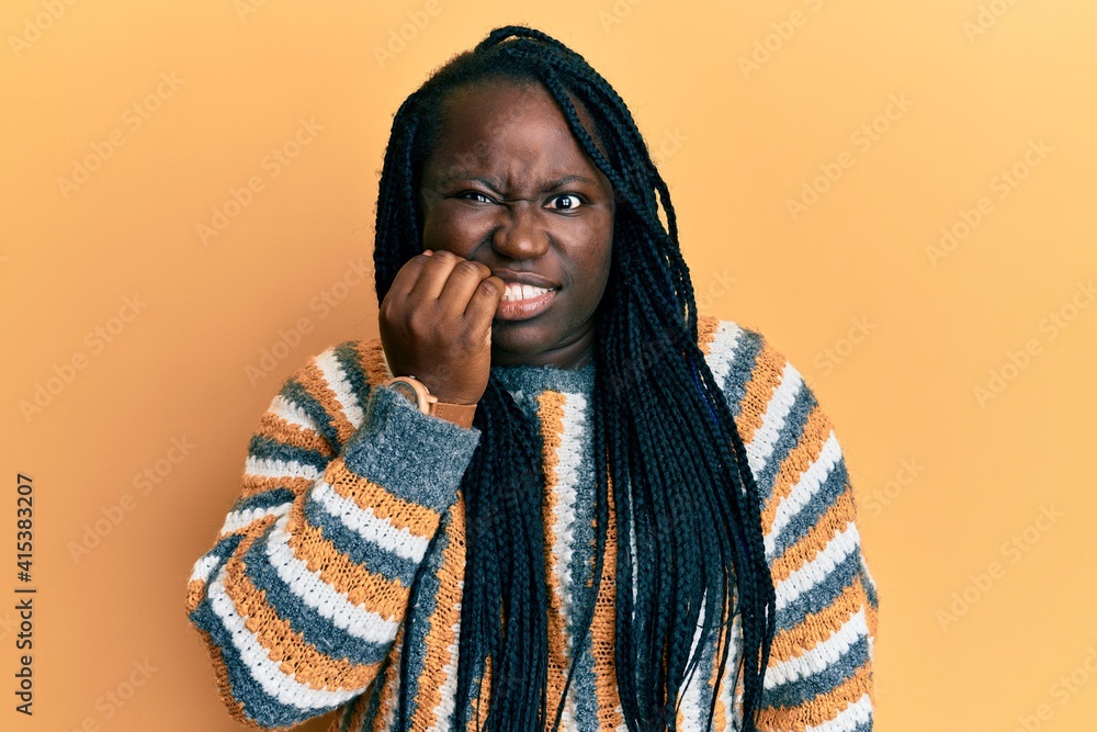 Young black woman with braids wearing casual winter sweater looking stressed and nervous with hands on mouth biting nails. anxiety problem. Young black woman with braids wearing casual winter sweater looking stressed and nervous with hands on mouth biting nails. anxiety problem.