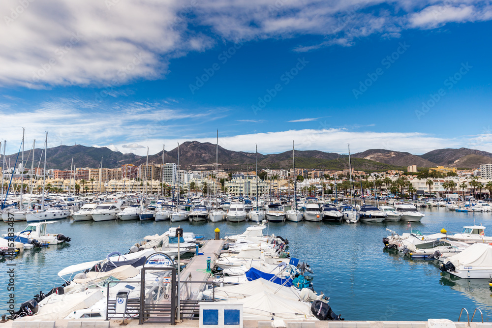 Beautiful Benalmadena touristic Harbour. Boats and yachts docked in the port. in background luxury urbanisations and hotels. Sunny summer day, blue sky with some clouds. 