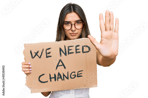 Wallpaper Mural Young hispanic woman holding we need a change banner with open hand doing stop sign with serious and confident expression, defense gesture Torontodigital.ca