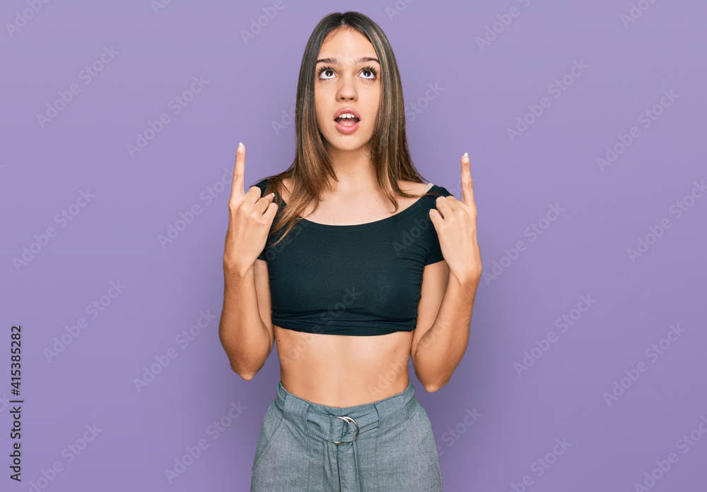 Young brunette woman wearing casual clothes amazed and surprised looking up and pointing with fingers and raised arms. Young brunette woman wearing casual clothes amazed and surprised looking up and pointing with fingers and raised arms.