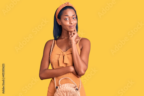 Young african american woman wearing summer outfit looking confident at the camera with smile with crossed arms and hand raised on chin. thinking positive. photo