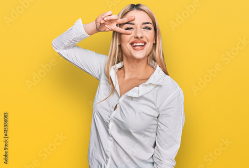 Young caucasian woman wearing casual clothes doing peace symbol with fingers over face, smiling cheerful showing victory