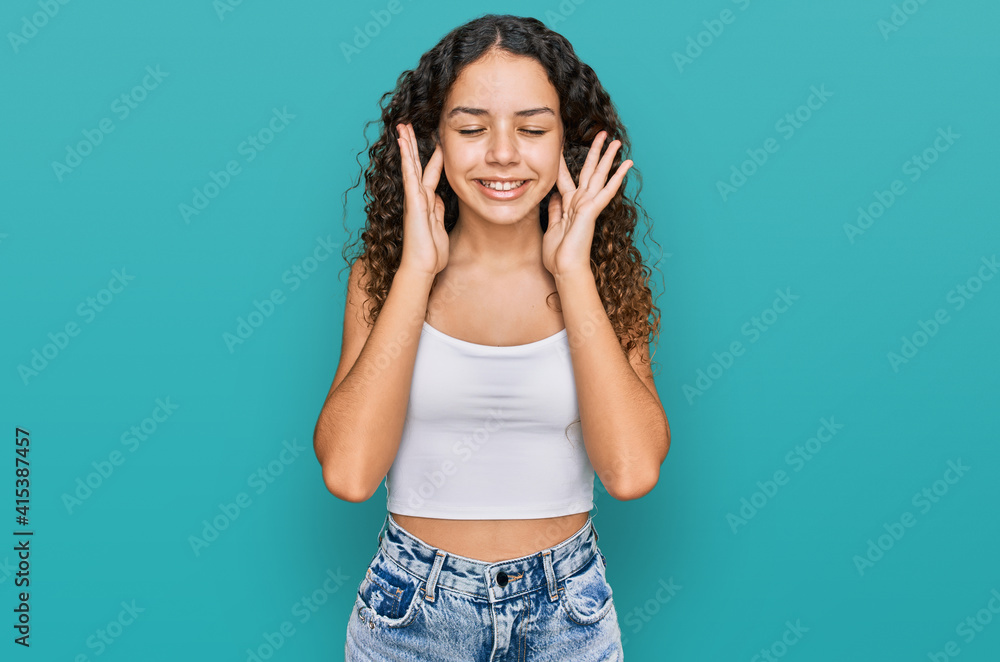 Teenager hispanic girl wearing casual clothes covering ears with fingers with annoyed expression for the noise of loud music. deaf concept. Teenager hispanic girl wearing casual clothes covering ears with fingers with annoyed expression for the noise of loud music. deaf concept.