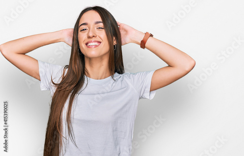 Young hispanic girl wearing casual white t shirt relaxing and stretching, arms and hands behind head and neck smiling happy © Krakenimages.com