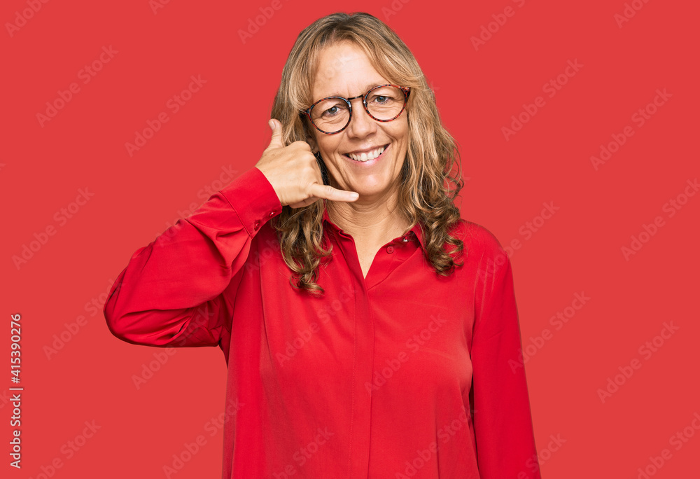 Middle age blonde woman wearing casual shirt over red background smiling doing phone gesture with hand and fingers like talking on the telephone. communicating concepts.