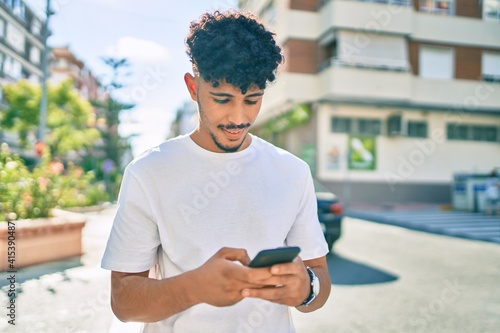 Tablou canvas Young arab man smiling happy using smartphone walking at city.