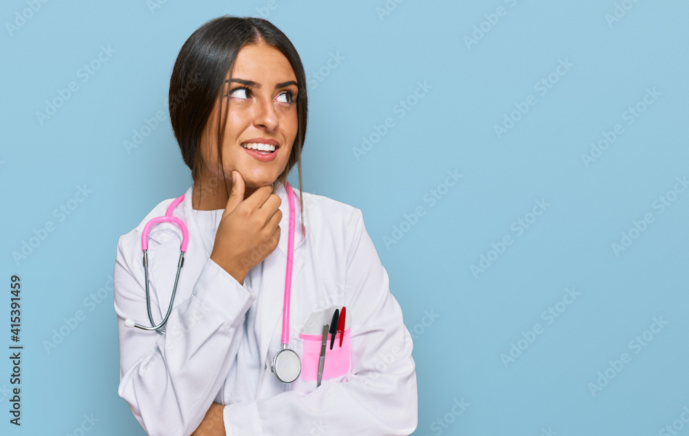 Beautiful hispanic woman wearing doctor uniform and stethoscope with hand on chin thinking about question, pensive expression. smiling with thoughtful face. doubt concept. Beautiful hispanic woman wearing doctor uniform and stethoscope with hand on chin thinking about question, pensive expression. smiling with thoughtful face. doubt concept.