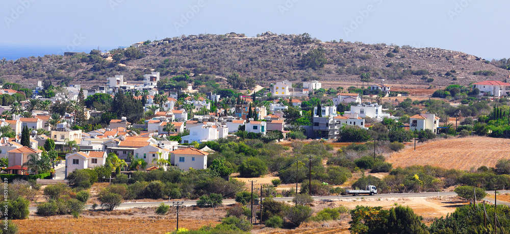 Rising mountain over residential buildings and a road with a passing car. Standard Mediterranean landscape. Rest in Cyprus. For wallpapers and backgrounds. Rising mountain over residential buildings and a road with a passing car. Standard Mediterranean landscape. Rest in Cyprus. For wallpapers and backgrounds.
