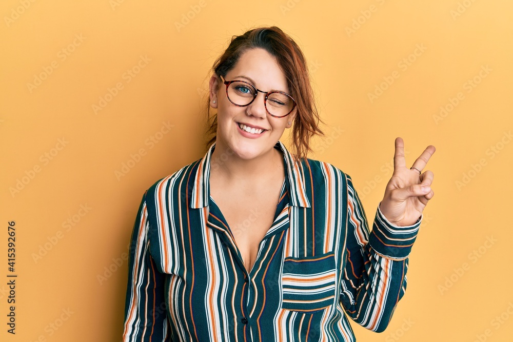Young caucasian woman wearing casual clothes and glasses smiling with happy face winking at the camera doing victory sign. number two. Young caucasian woman wearing casual clothes and glasses smiling with happy face winking at the camera doing victory sign. number two.