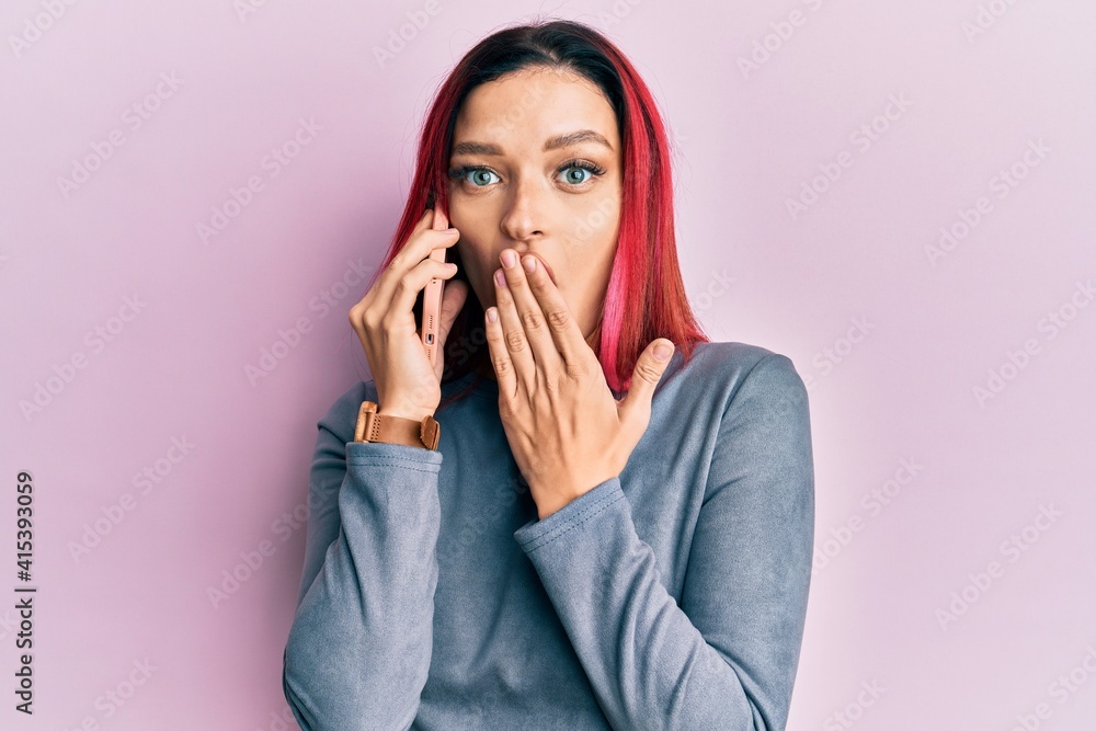 Young caucasian woman having conversation talking on the smartphone covering mouth with hand, shocked and afraid for mistake. surprised expression Young caucasian woman having conversation talking on the smartphone covering mouth with hand, shocked and afraid for mistake. surprised expression