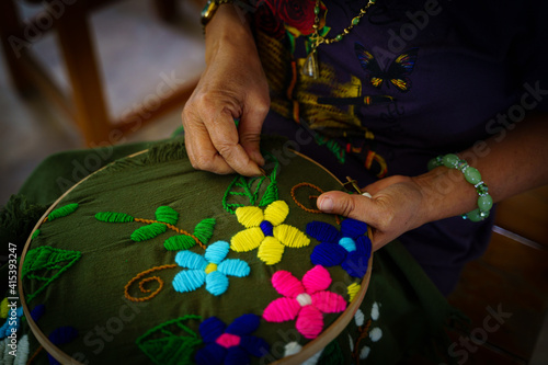 A woman embroider flower on green fabric by using needle. 