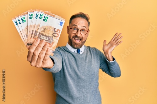 Cuadro en lienzo Handsome middle age man holding bunch of euros celebrating achievement with happ