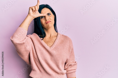 Young caucasian woman wearing casual clothes making fun of people with fingers on forehead doing loser gesture mocking and insulting.