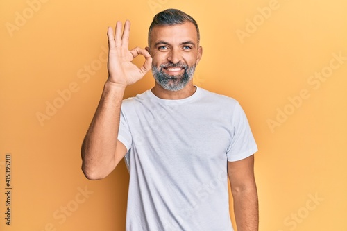 Middle age handsome man wearing casual white tshirt smiling positive doing ok sign with hand and fingers. successful expression. © Krakenimages.com