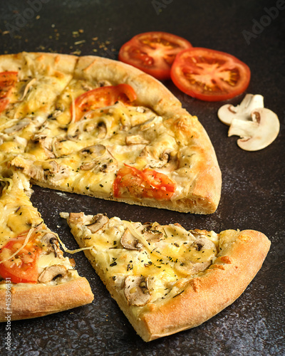 pizza and cut-out slice close-up on a dark background with ingredients spread out