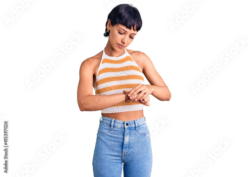 Young brunette woman with short hair wearing casual clothes checking the time on wrist watch, relaxed and confident