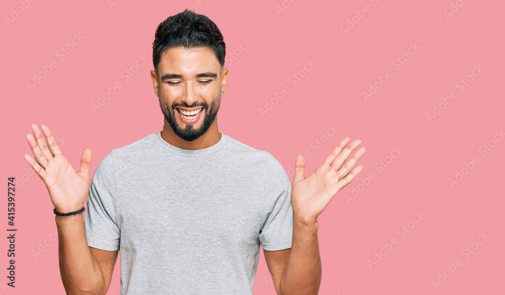Fototapeta premium Young man with beard wearing casual grey tshirt celebrating mad and crazy for success with arms raised and closed eyes screaming excited. winner concept