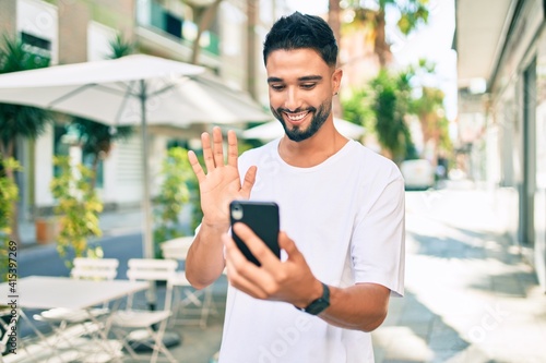 Young arab man smiling happy doing video call using smartphone at the city. © Krakenimages.com
