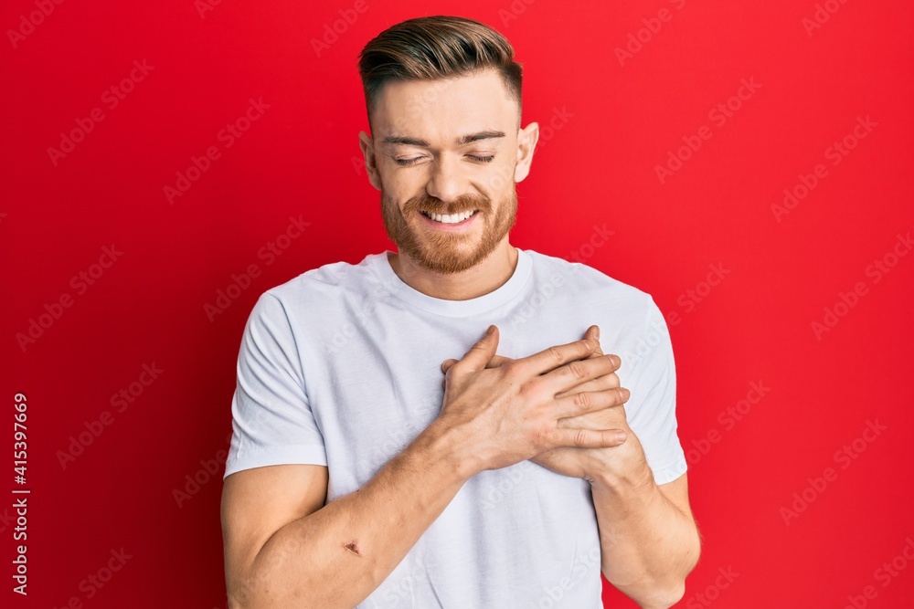 Young redhead man wearing casual white t shirt smiling with hands on chest, eyes closed with grateful gesture on face. health concept. Young redhead man wearing casual white t shirt smiling with hands on chest, eyes closed with grateful gesture on face. health concept.