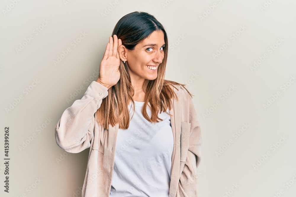 Brunette young woman wearing casual clothes smiling with hand over ear listening an hearing to rumor or gossip. deafness concept. Brunette young woman wearing casual clothes smiling with hand over ear listening an hearing to rumor or gossip. deafness concept.