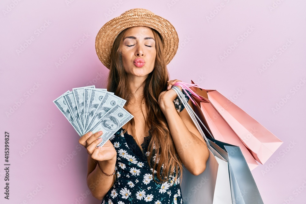 Young brunette woman holding shopping bags and dollars looking at the camera blowing a kiss being lovely and sexy. love expression.