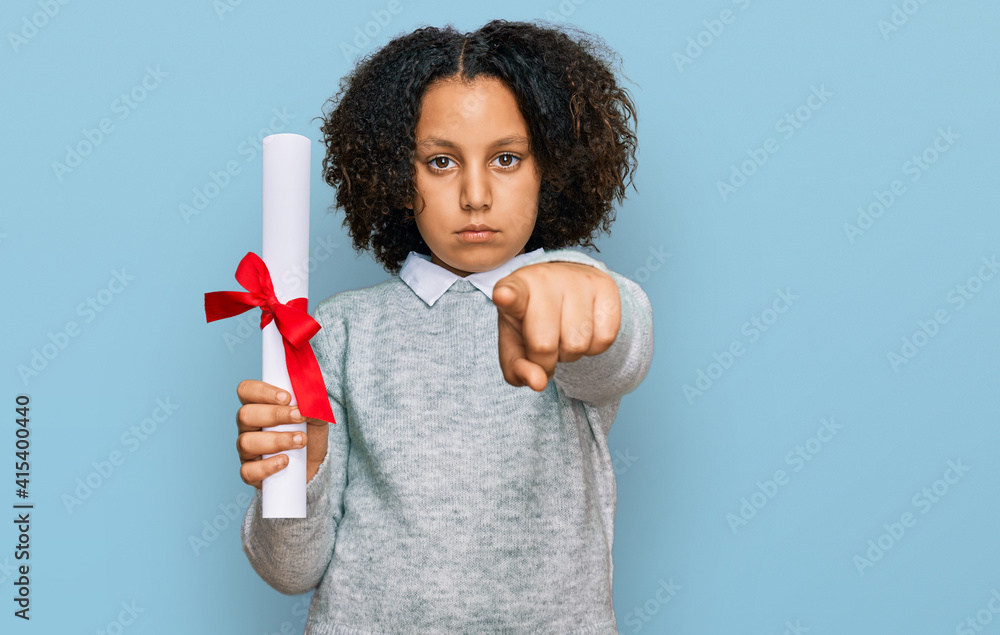 Young little girl with afro hair holding graduate degree diploma pointing with finger to the camera and to you, confident gesture looking serious Young little girl with afro hair holding graduate degree diploma pointing with finger to the camera and to you, confident gesture looking serious