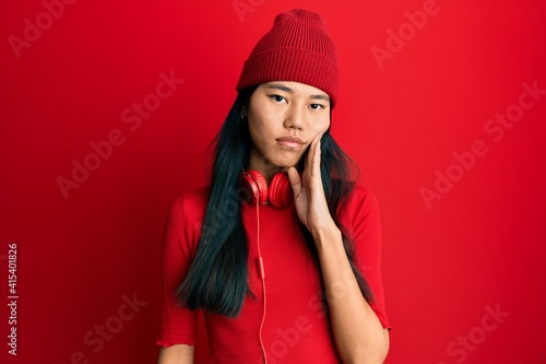 Young chinese woman listening to music using headphones touching mouth with hand with painful expression because of toothache or dental illness on teeth. dentist