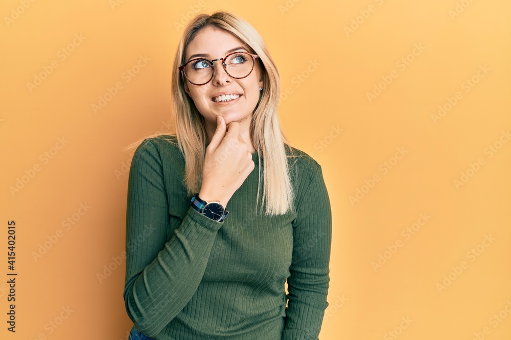 Young caucasian woman wearing casual clothes and glasses with hand on chin thinking about question, pensive expression. smiling with thoughtful face. doubt concept.