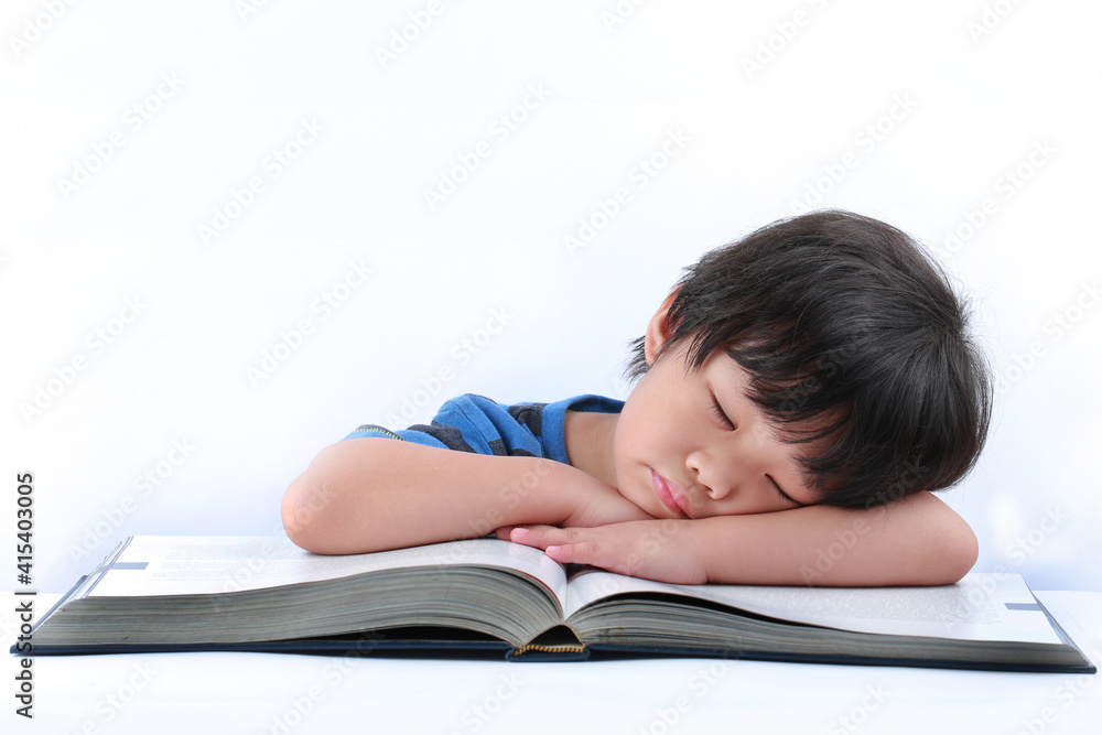 A tired little Asian boy resting his head on his arms as he sits at his desk looking bored while reading a book. A tired little Asian boy resting his head on his arms as he sits at his desk looking bored while reading a book.