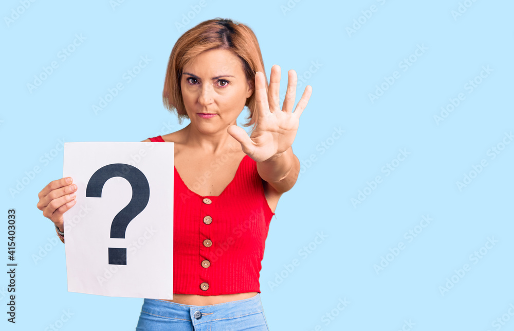 Young blonde woman holding question mark with open hand doing stop sign with serious and confident expression, defense gesture Young blonde woman holding question mark with open hand doing stop sign with serious and confident expression, defense gesture