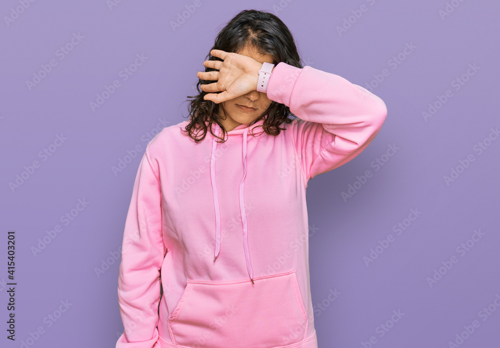 Young hispanic woman wearing casual sweatshirt covering eyes with arm, looking serious and sad. sightless, hiding and rejection concept Young hispanic woman wearing casual sweatshirt covering eyes with arm, looking serious and sad. sightless, hiding and rejection concept