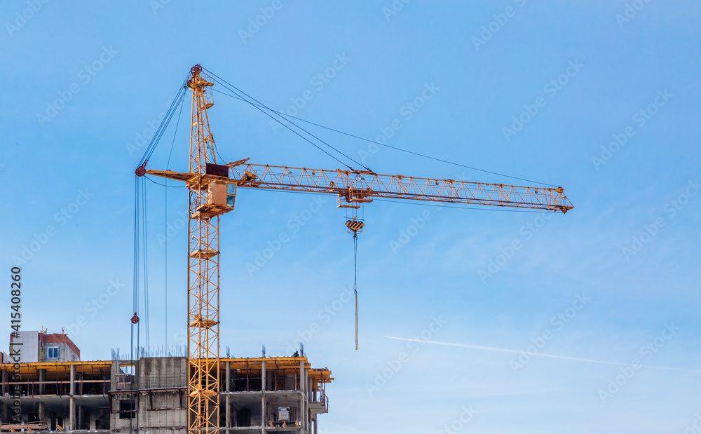 Construction cranes and unfinished apartment building against the blue sky. Housing construction. Construction cranes and unfinished apartment building against the blue sky. Housing construction.