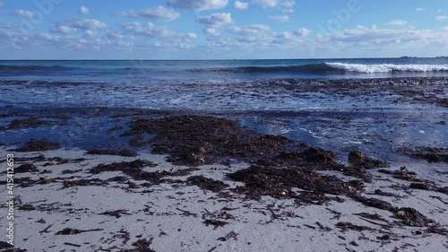 Small waves roll onto the shore with bundles of algae. Villasimius, Sardinia island
