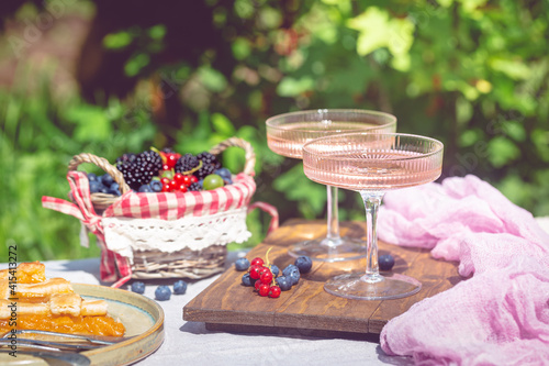Outdoor summer lifestyle with a gourmet picnic laid out in a garden with berries, pie and pink drink in stylish glasses