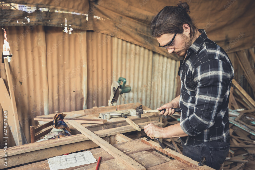 male carpenter using hammer and chisel on a piece of wood in workshop(vintage tone)
