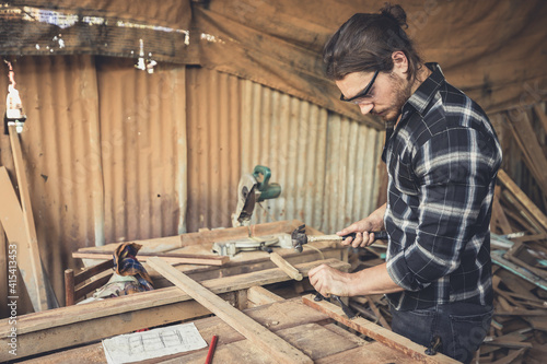 male carpenter using hammer and chisel on a piece of wood in workshop(vintage tone)